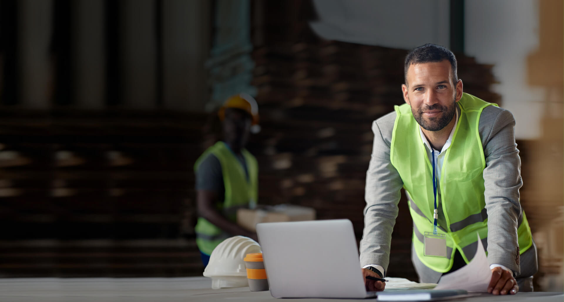 Male warehousing business owner working on laptop with warehouse and employee in background