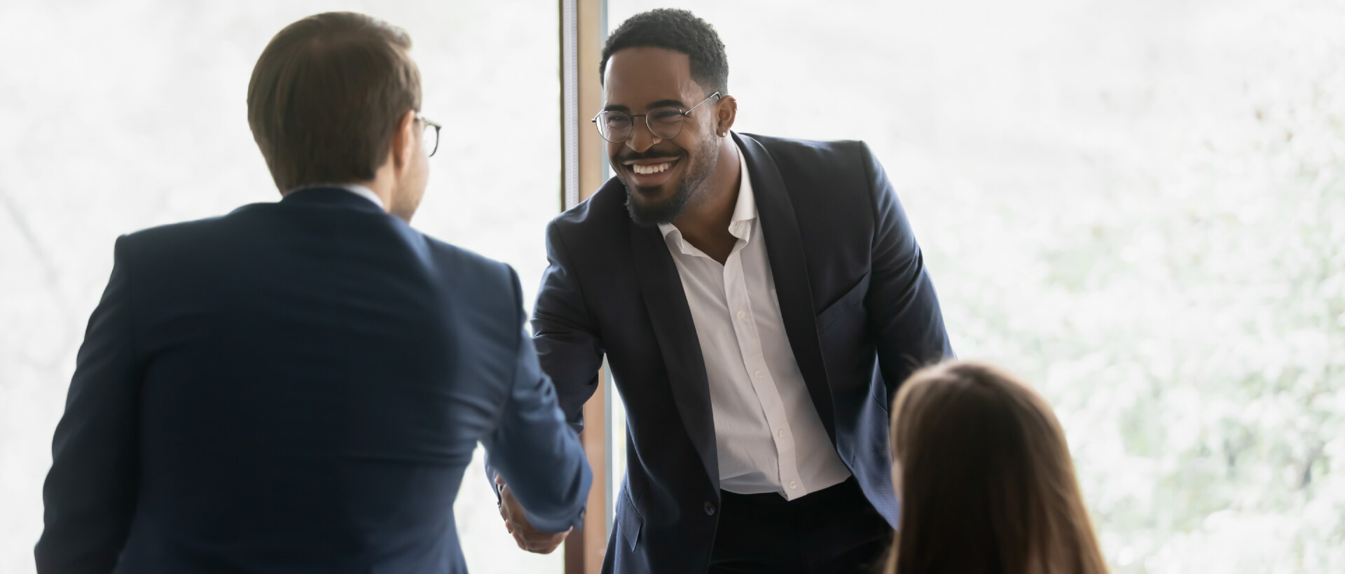 Young business man standing and shaking hands with another business man across the table