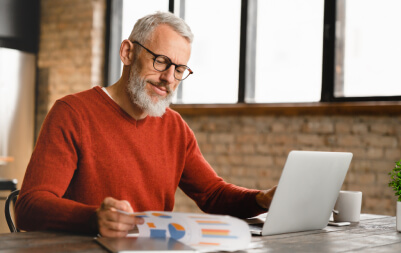 Middle aged bearded man working on laptop and looking a paper reports