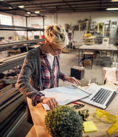 Female woodworker looking at drawings in her shop