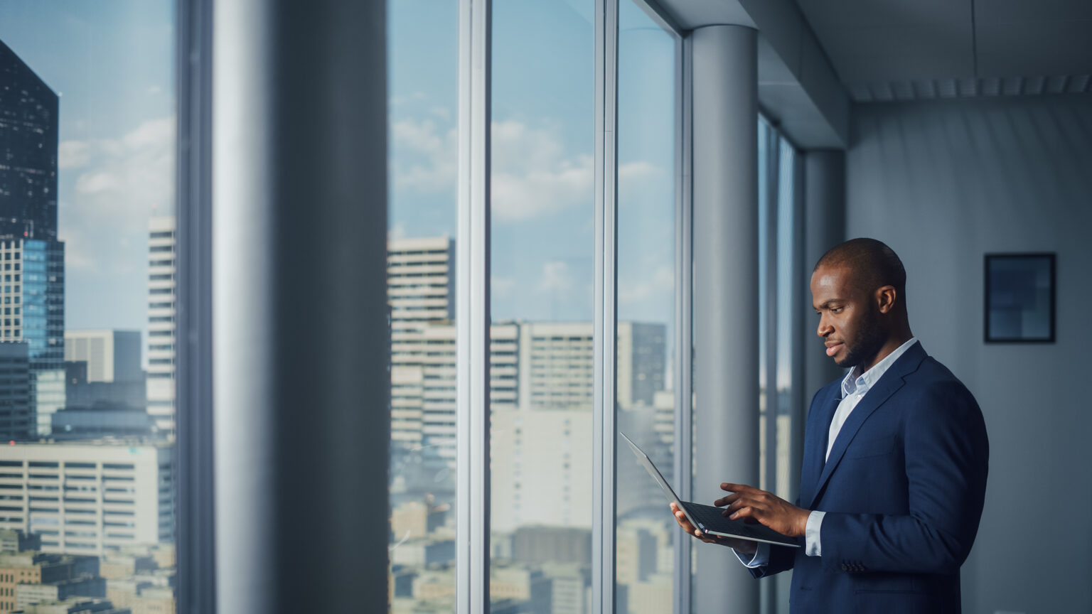 Thoughtful Black Businessman in a Tailored Suit Using Laptop whi
